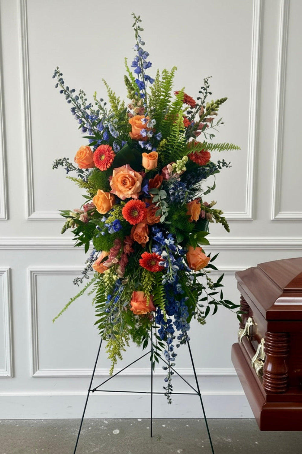bright summer flowers designed in a standing funeral spray next to a casket