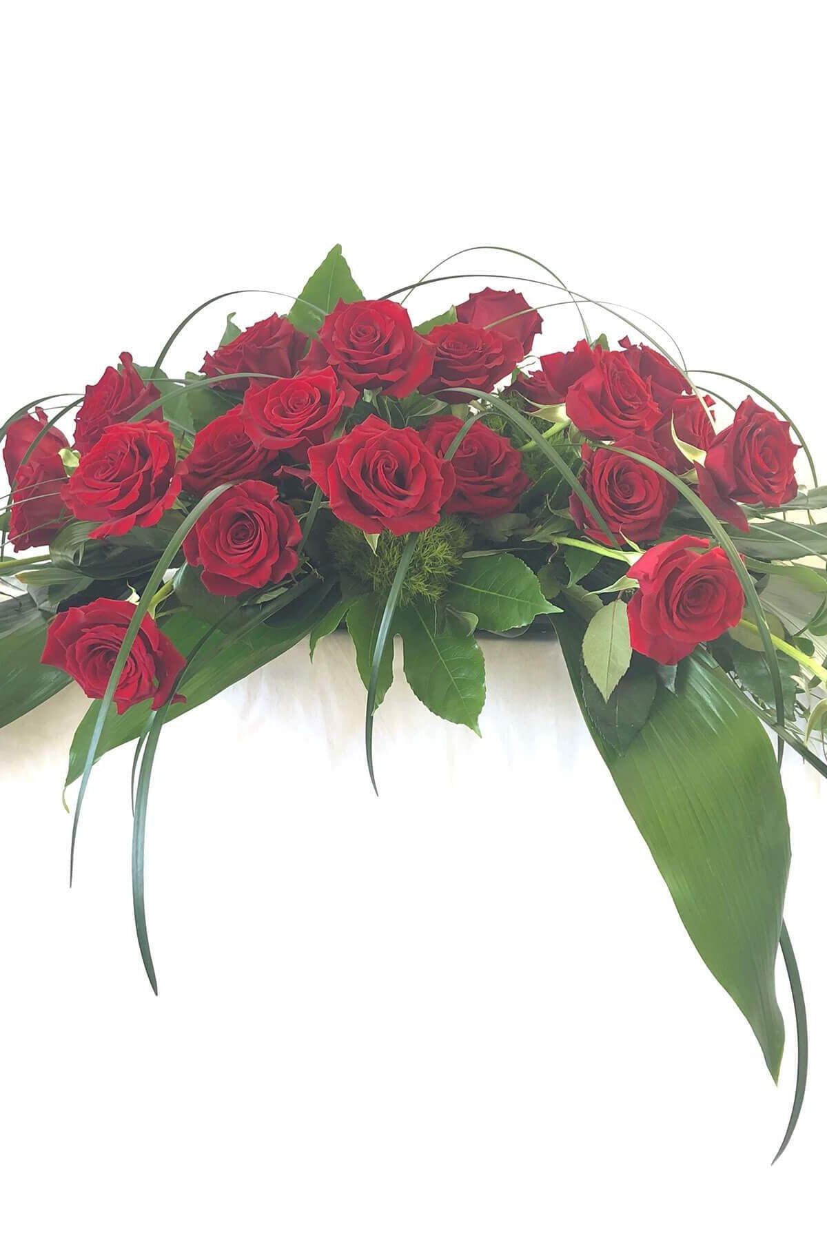 A floral casket spray with red roses, green foliage, and yellow leaves.
