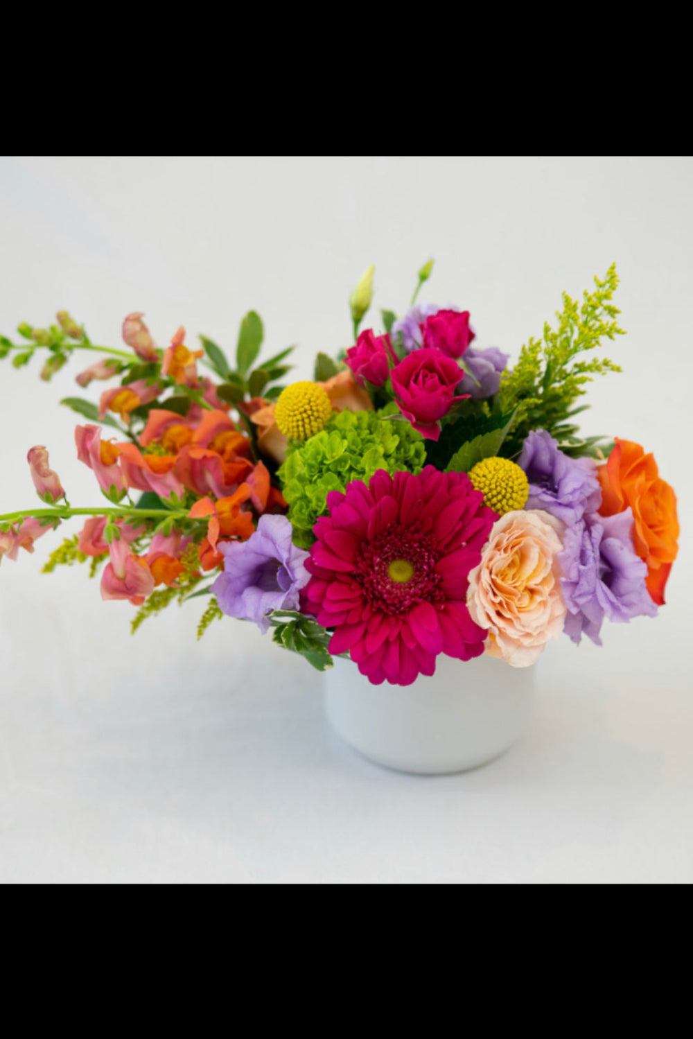 A colorful floral arrangement of various flowers in a white vase against a white background.